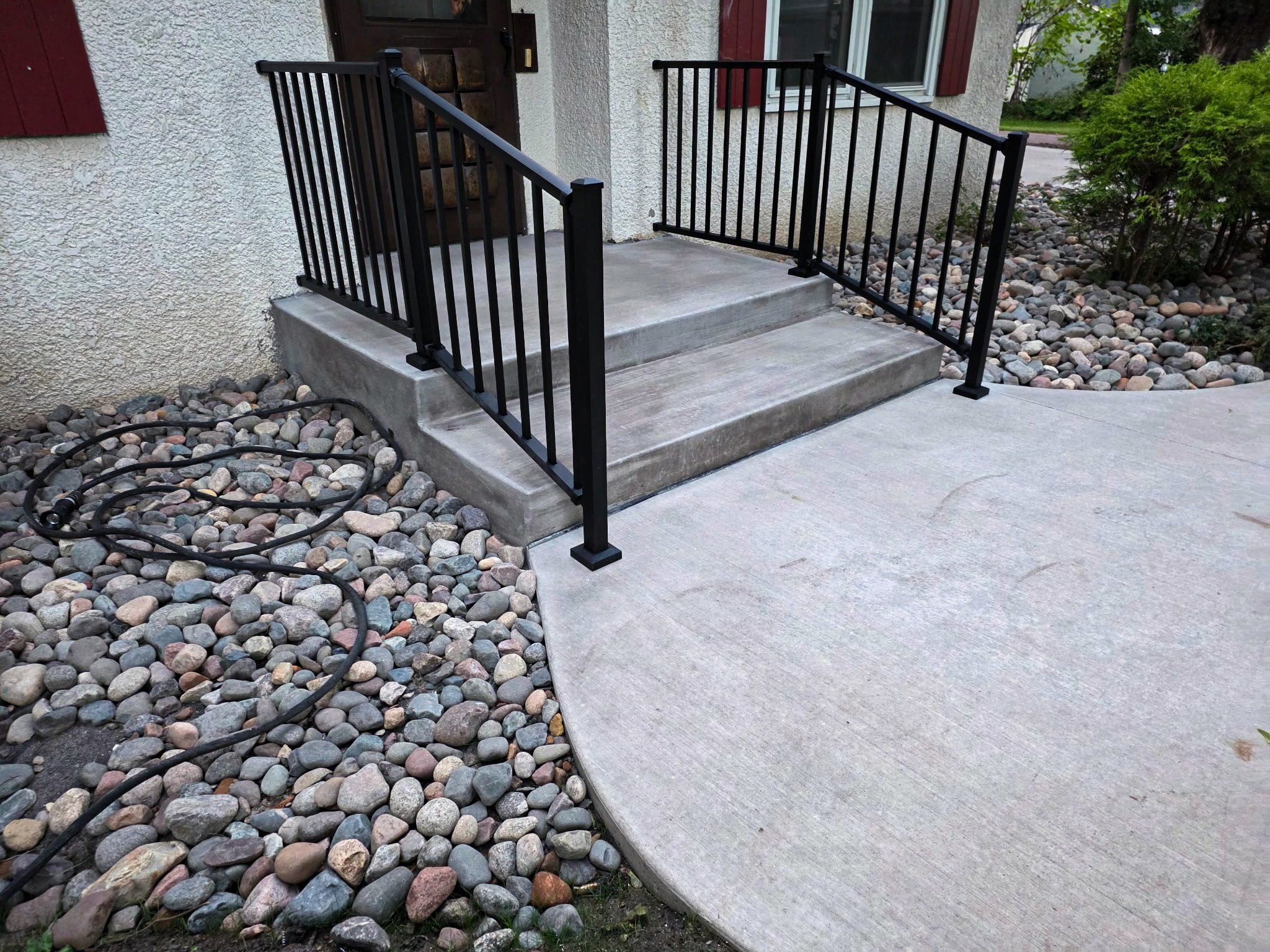 Finished concrete entrance with steps, landing, walkway, and black railings